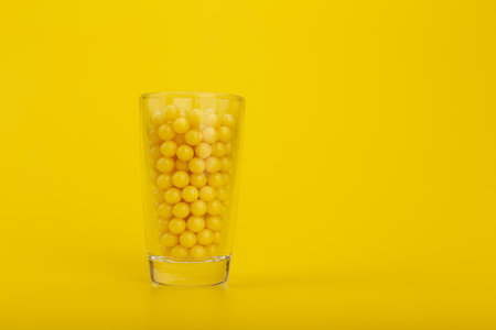 Transparent glass shot with vitamins on yellow background with space for textの写真素材