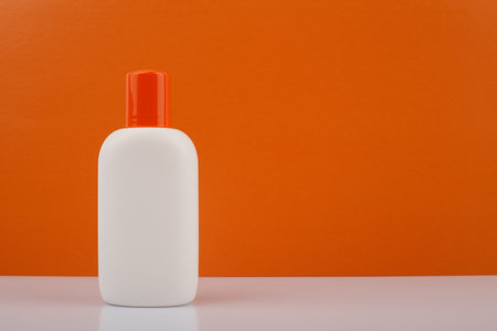 Sunscreen lotion against orange background with space for text