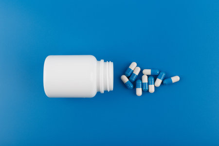 Flat lay with medication bottle and spilled pills on blue background. Concept of medication, vitamins or painkillersの写真素材