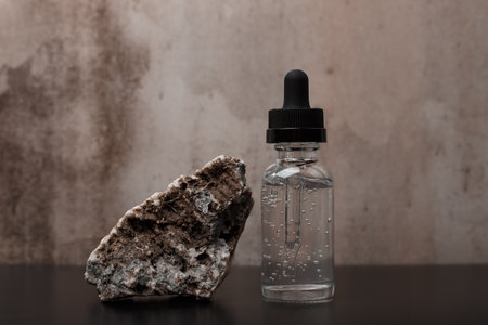 Beauty serum next to a stone on black table against dark marble background. Concept of luxury skincareの写真素材