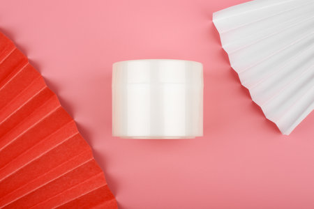 Flat lay with white glossy cream jar on pink background decorated with white and red waversの写真素材