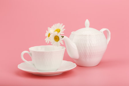 White tea pot with camomile flowers and tea cup on pink background. Concept of herbal tea and healthy lifestyleの写真素材