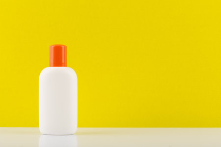 Sunscreen lotion for safe tanning on white table against yellow background with copy spaceの写真素材
