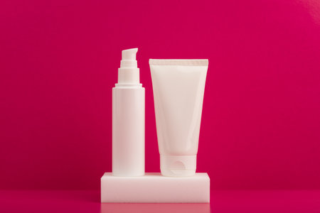 Two white unbranded cream tubes on white podium against pink background. Concept of skincare and beauty productsの写真素材