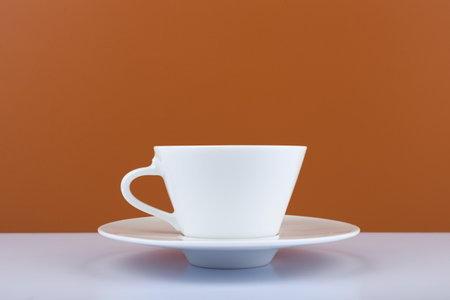 White glossy coffee cup on white table against brown background with copy spaceの写真素材