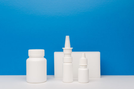 Medication bottle, nose spray and eye drops on white table against blue background with copy spaceの写真素材