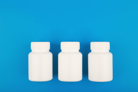 Flat lay with three white medication bottles in a row on blue background with copy spaceの写真素材