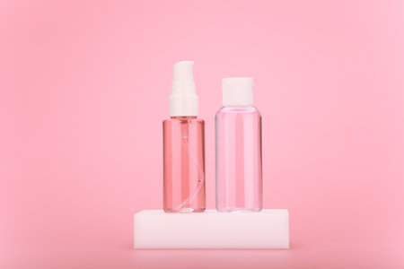 Cleaning foam or gel and moisturizing skin lotion in transparent bottle on white podium against bright pink backgroundの写真素材