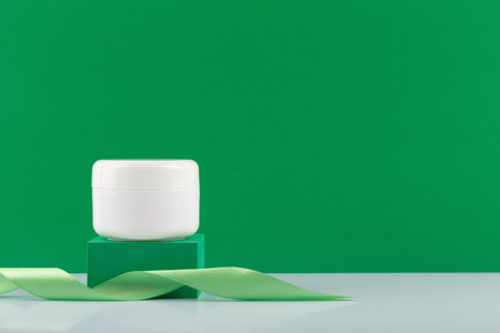 White cream, mask or balm jar on green podium with a ribbon against green background with copy spaceの写真素材