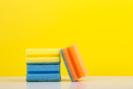 Colorful sponges for washing dishes on white table against yellow background with copy spaceの写真素材