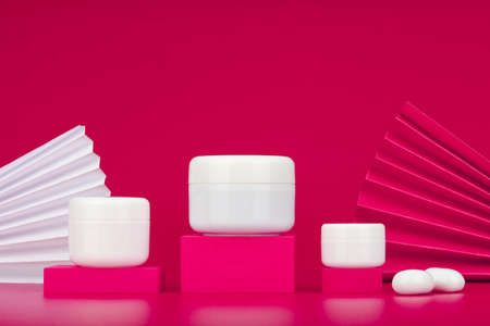 Unbranded cosmetic jars on pink podiums against pink background decorated with wavers and white stonesの写真素材