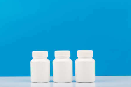 Three white medication bottles against blue background. Concept of vitamins, supplements, medication and healthcareの写真素材