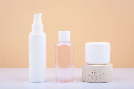 Set of cosmetic bottles with face cream, lotion and lip balm on white table against beige backgroundの写真素材