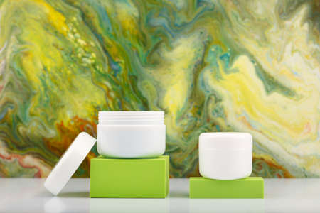 Two white cosmetic jars on green podiums against green marbled background with copy spaceの写真素材