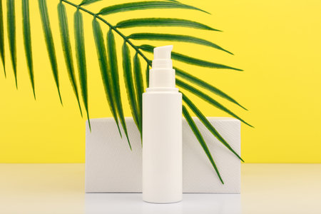 Summer face cream with SPF with white geometric podium and palm leaf against yellow background. Concept of sunblockの写真素材