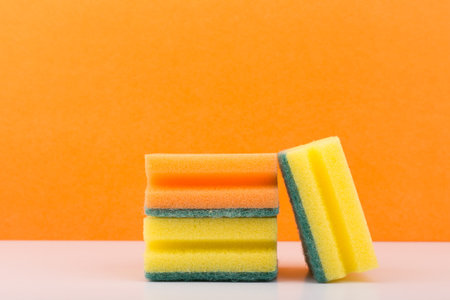 Yellow and orange sponges for house cleaning and dish washing on white table against orange backgroundの写真素材