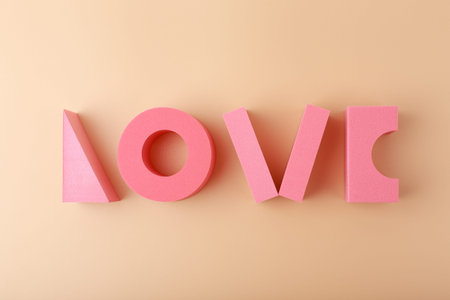 Creative flat lay of word love made of pink geometric figures against light beige background.