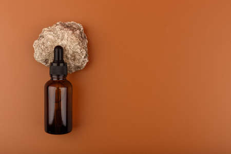 Top view of beauty serum in dark bottle on natural stone on brown background with copy spaceの写真素材