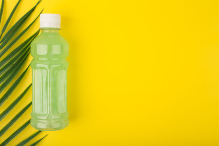 Green organic detox lemonade on yellow background with copy space decorated with palm leaf