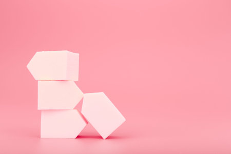 Stack of white make up sponges on pink background with copy space