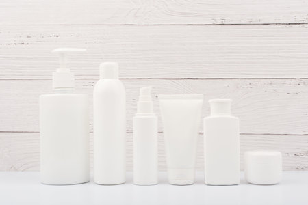 Set of white unbranded cosmetic bottles for face and body care in a row against white wooden...