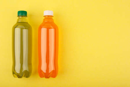 Orange and green refreshing soda drinks in plastic bottles on yellow backgroundの写真素材