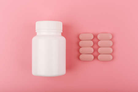 White medication bottle with pink pills spilled in a row against pink backgroundの写真素材