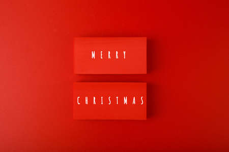 Minimal flat lay Christmas theme. Merry Christmas written on two red tablets on red background. Creative layout in red colorsの写真素材