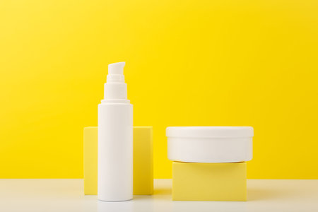 Face cream and body cream in white tubes with geometric props against yellow background. Concept of beauty products for face and body care