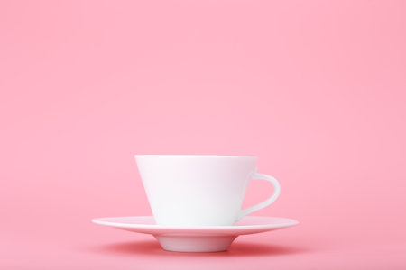 Close up of white ceramic coffee or tea cup with saucer isolated on bright pink background with copy space. Trendy concept of hot drinks and kitchenwareの写真素材