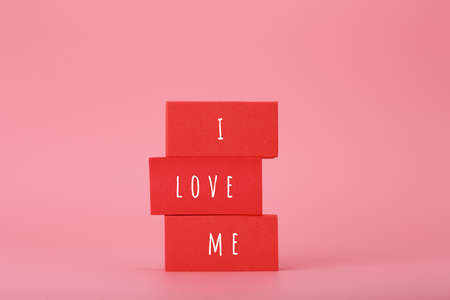 I love me creative concept of self love and mental health or being single. Stack of red blocks against pink backgroundの写真素材