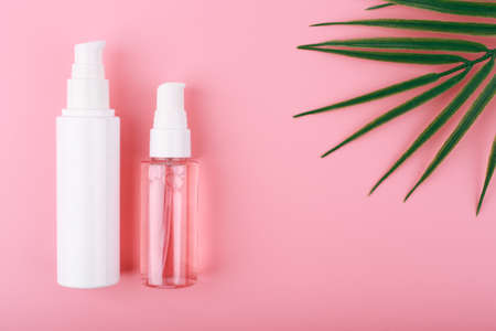 Set of cosmetic bottles for face cleansing, exfoliating and moisturizing against pink background with copy space and palm leaf. Trendy modern flat lay with a set of beauty products for daily useの写真素材