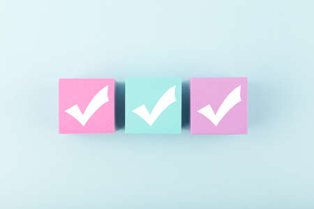 Three checkmarks on multicolored cubes in a row in the middle of bright pastel blue background. Concept of questionary, checklist, to do list, planning, business or verification. Modern minimal compositionの写真素材