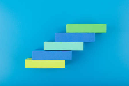 Ladder of success modern and trendy business or personal development concept. Top view of ladder made of multicolored rectangles with space for text against blue backgroundの写真素材