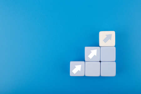 Ladder career, sales or business growth and success path concept. Blue blocks as step stairs with white arrows up on blue background with copy spaceの写真素材