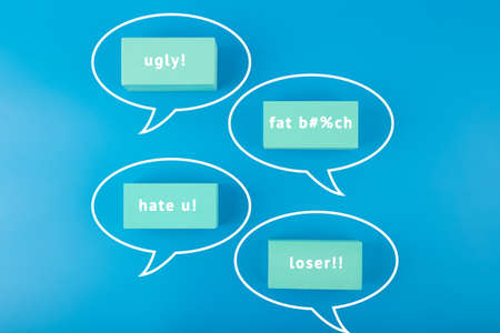 Creative cyberbullying concept. Minimal flat lay with negative, insulting messages in speech bubbles on blue background.の写真素材