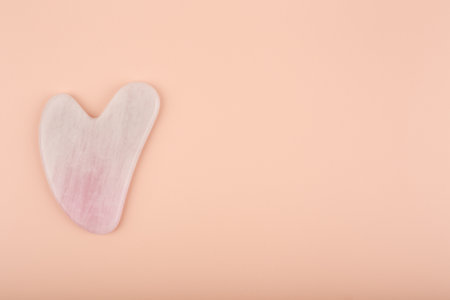 Top view of pink heart shaped guasha stone made of quartz crystal on bright beige background with copy space. Concept of alternative skin care treatment, self massage and acupressureの写真素材