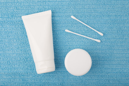 Creative flat lay with face cream or shaving foam, under eye cream or lip balm and cotton swabs on blue fleecy towel. Concept of hygiene, bath or man's skin care routineの写真素材
