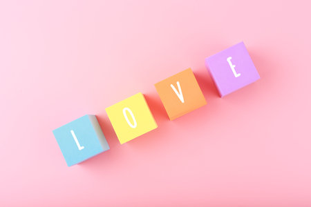 Word love written on colorful toy cubes against bright pink background with copy space. Minimal...