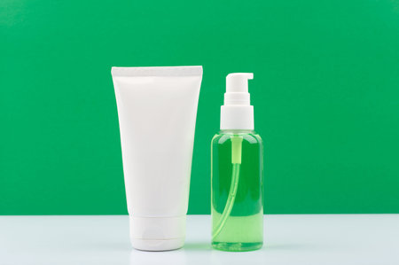 Cosmetic set with face cream and cleansing foam in transparent bottle on white table against green backgroundの写真素材