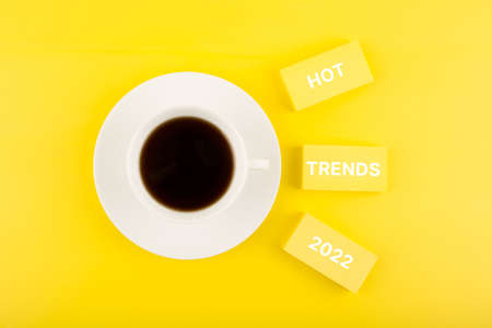 Hot trends 2022 written on rectangles next to cup of coffee on bright yellow backgroundの写真素材