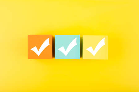 Three checkmarks on colorful blocks against bright yellow backgroundの写真素材