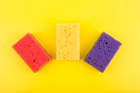 Close up of three multicolored red, purple and yellow cleaning sponges on bright yellow background