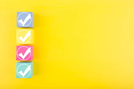 Four white checkmarks in a row on colorful toy cubes against bright yellow background with copy spaceの写真素材