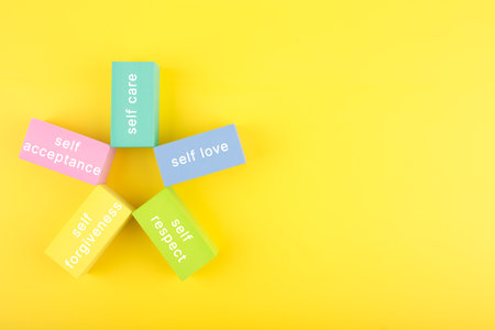Mental health formula concept. Self acceptance, self care, self respect and self forgiveness written on flower from multicolored rectangles on yellow background with copy spaceの写真素材