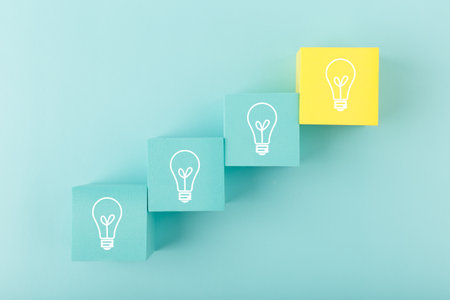 Creativity concept. Light bulbs on blue and yellow toy cubes as a ladder on blue background. Brainstorming and idea developingの写真素材