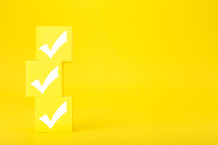 Three white checkmarks on stack of yellow toy cubes on bright yellow background with copy space. Concept of questionary, kids related checklist, to do list, planning, business or verification.の写真素材
