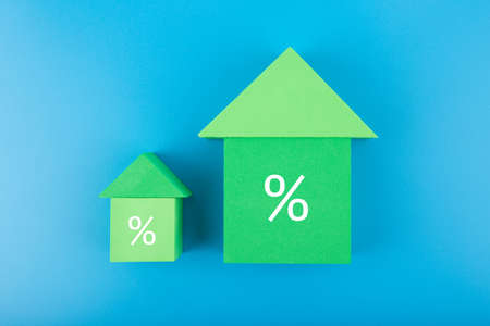 Two green houses made of toy blocks with increasing percentage sign on blue backgroundの写真素材