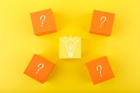 Creativity, innovation and idea concept. Flat lay with light bulb drawn on yellow cube and question...