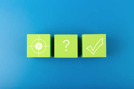 Concept of scoring a goal. Target, question sign and checkmark on green toy cubes on blue backgroundの写真素材